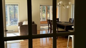 Una habitación amplia con piso de madera, una zona de comedor con mesa y sillas, y vista al exterior a través de grandes ventanas.