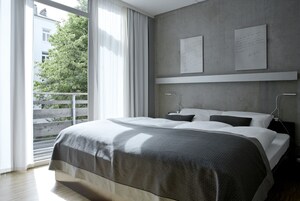 Un dormitorio moderno con una cama grande, un balcón y vistas a un árbol y un edificio.