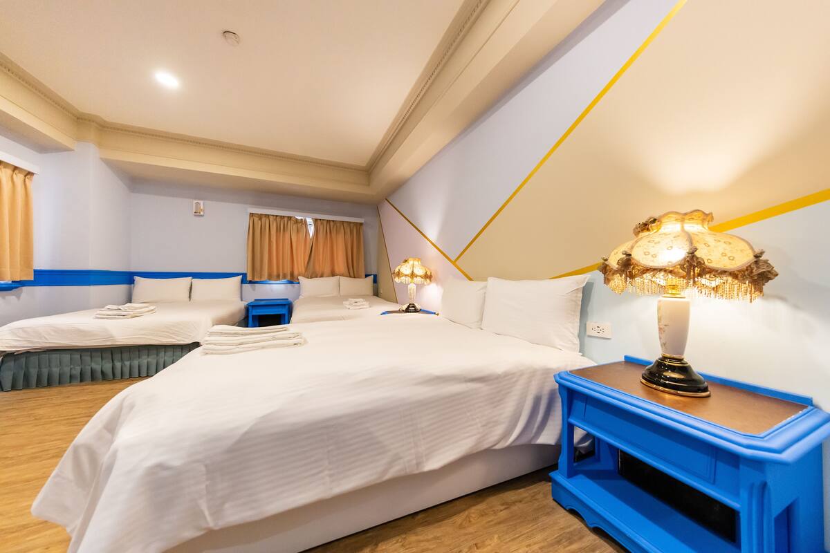 A hotel room with two beds, a blue nightstand, and a decorative lamp.