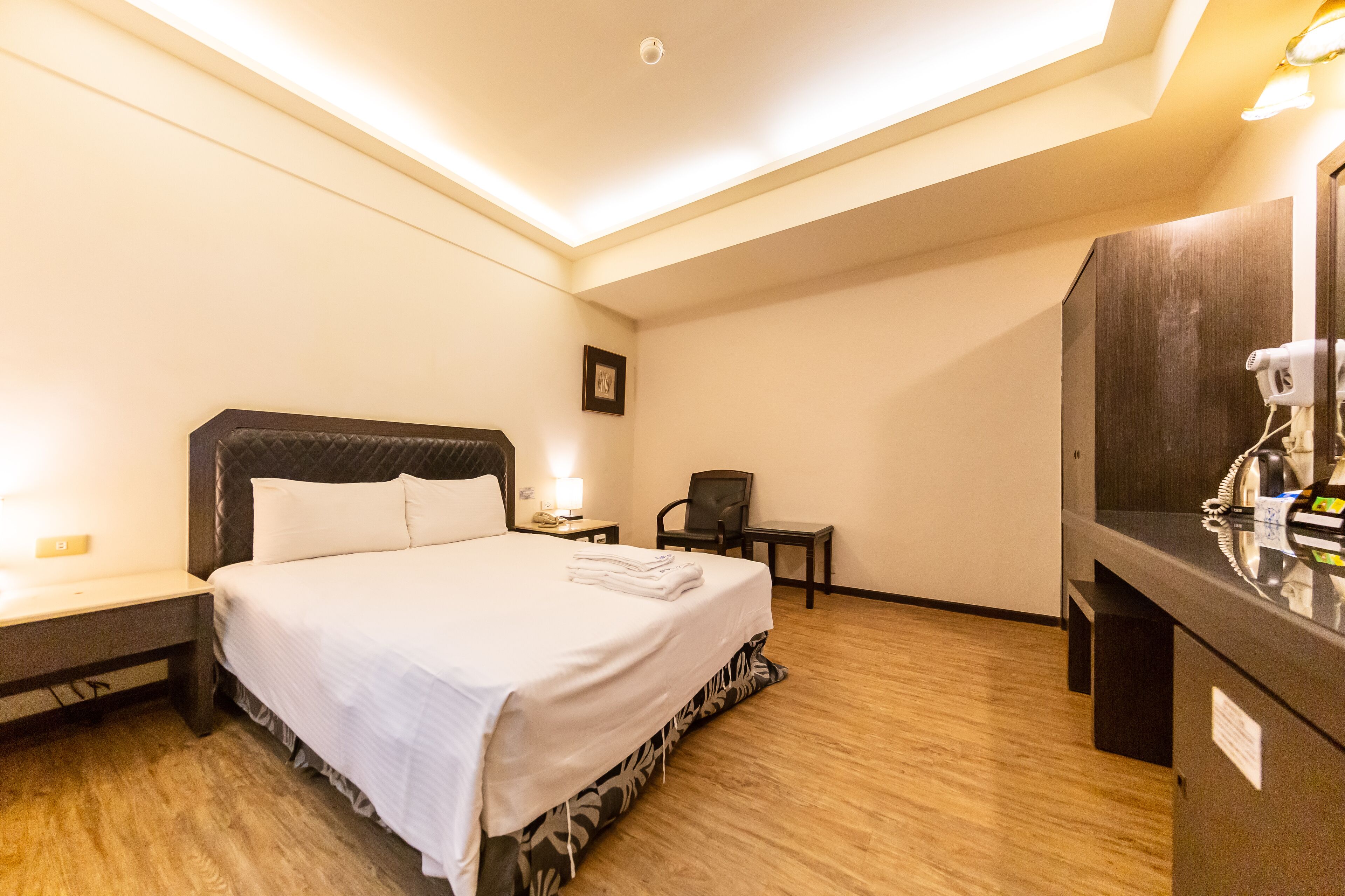 A hotel room with a bed, a desk, a chair, a mirror, and a hairdryer.