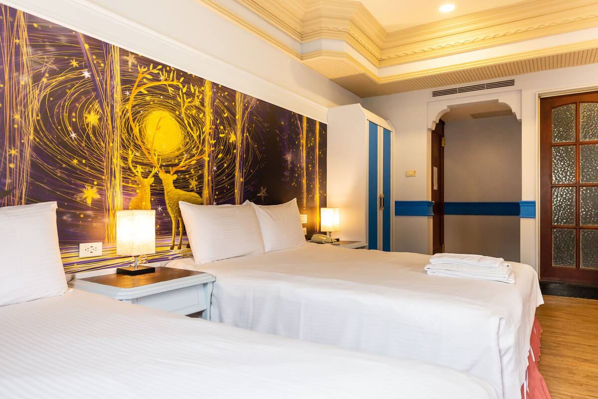 A hotel room with two beds, a large wall mural, and a door with a blue stripe.