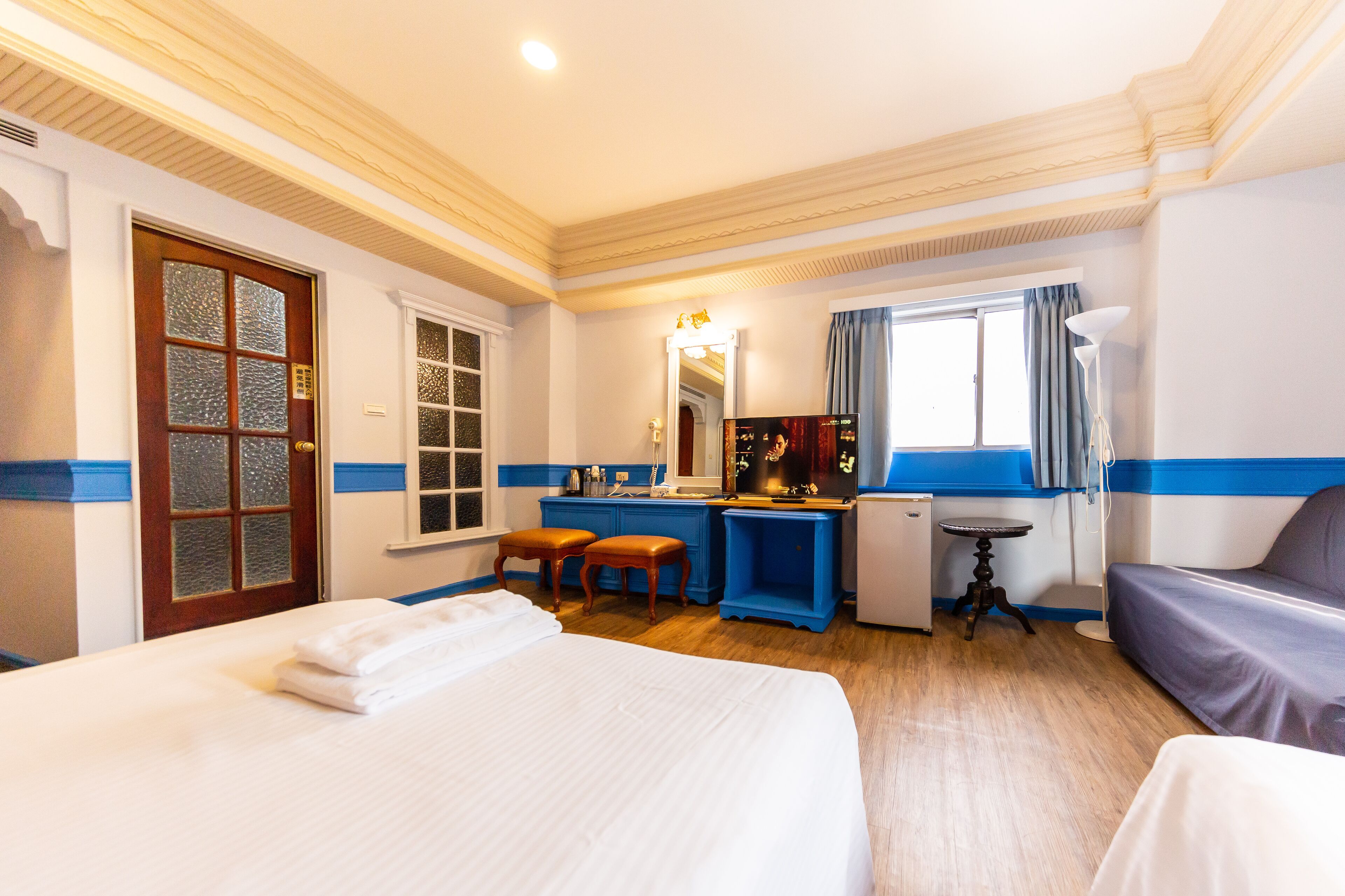 Een hotelkamer met een bed, een bureau, een stoel, een tafeltje, een lamp en een raam met gordijnen.