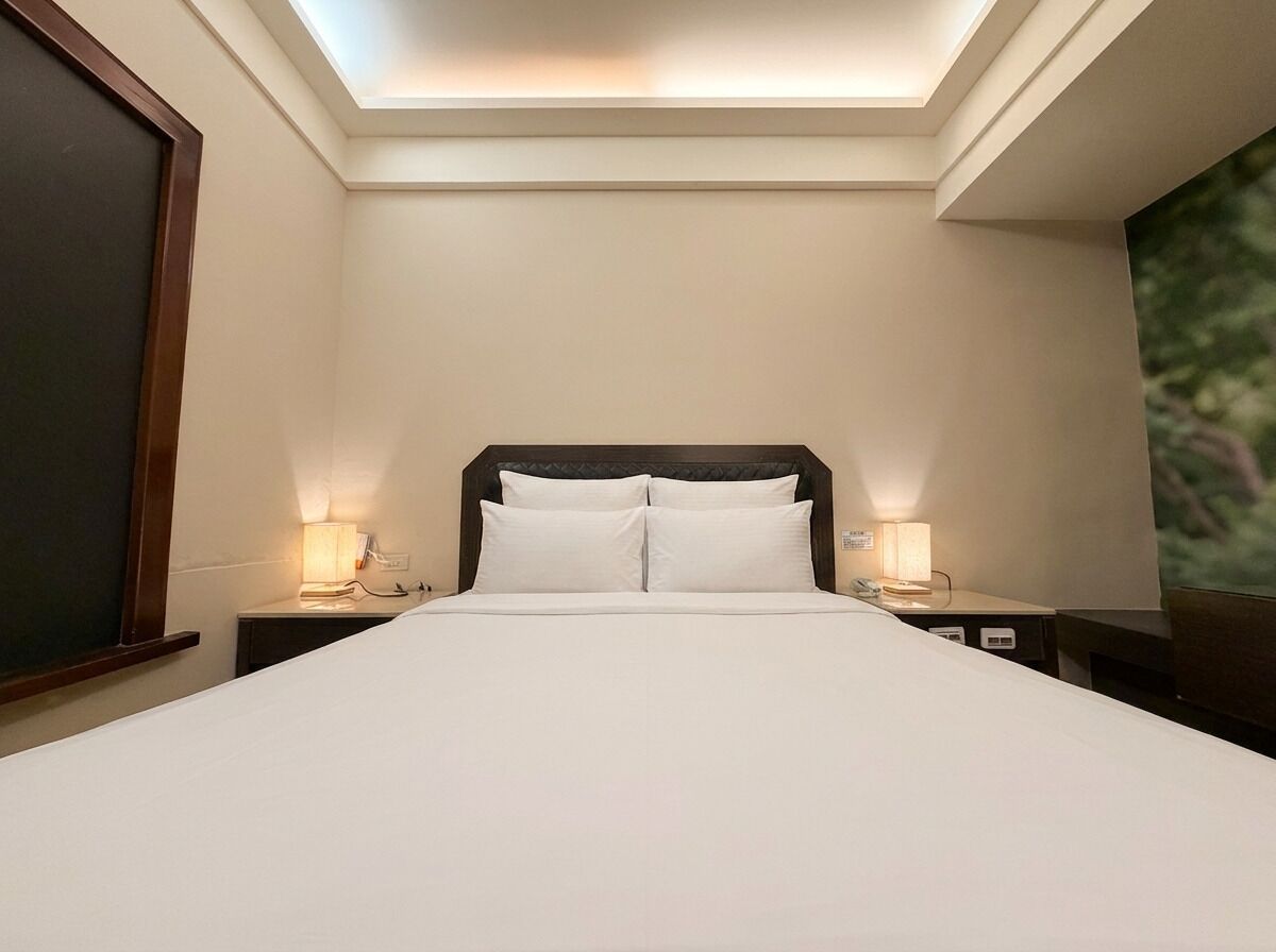A hotel room with a skylight, a large bed with white linens, two bedside lamps, and a nightstand with a phone.