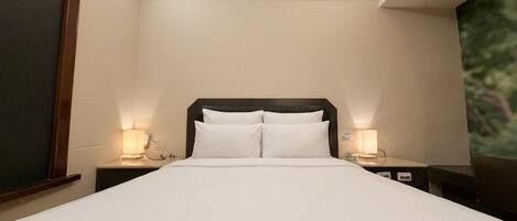A hotel room with a skylight, a large bed with white linens, two bedside lamps, and a nightstand with a phone.