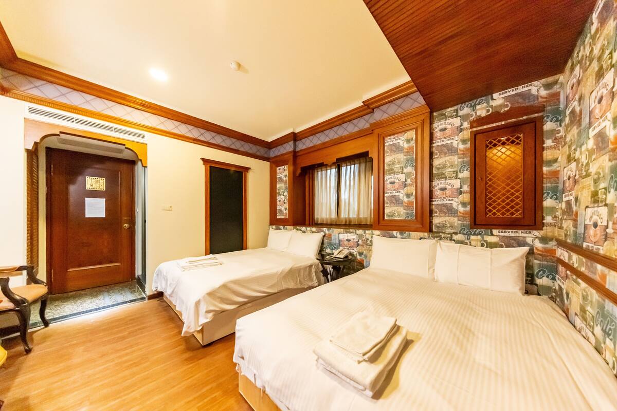 A hotel room with two beds, a wooden door, a small table, and a chair.