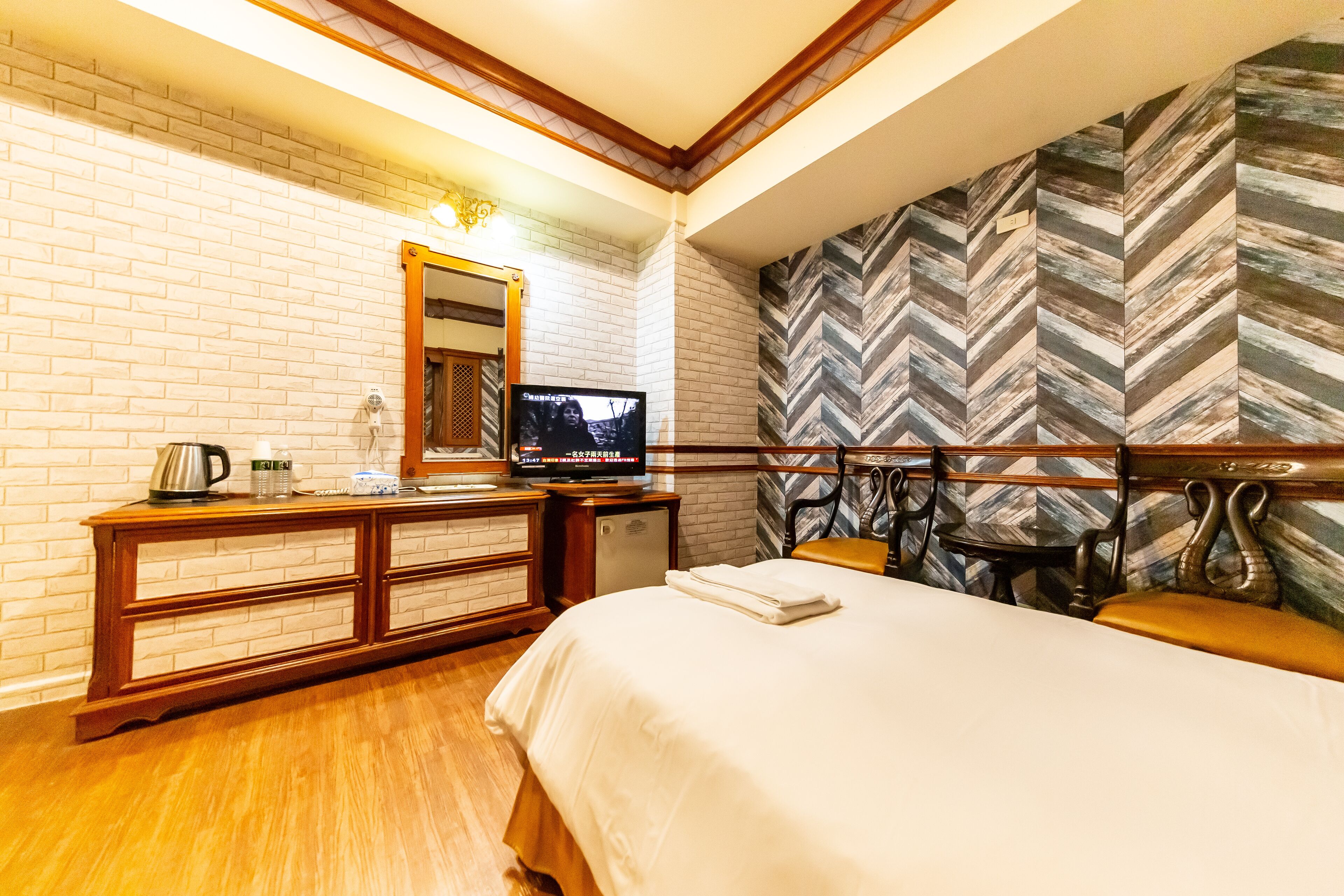 Quarto de hotel com parede de tijolos, cômoda de madeira, televisão e cama com colcha branca.