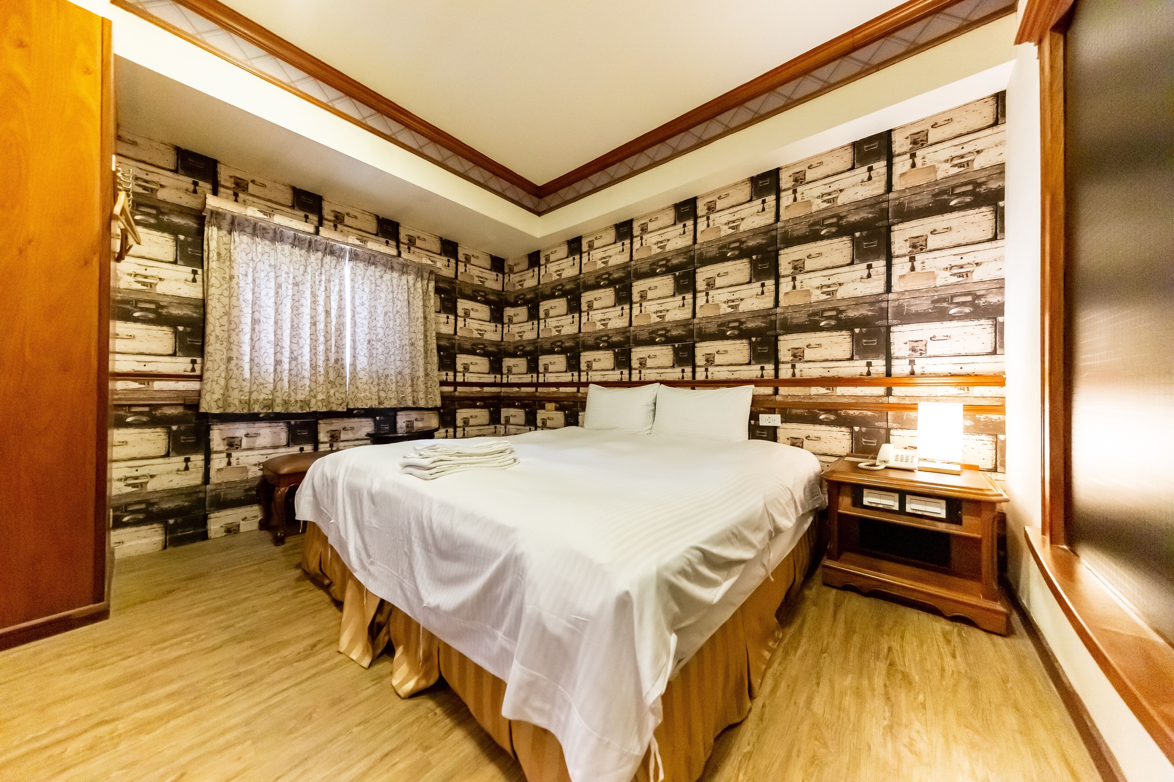A bedroom with a large bed, wooden headboard, a nightstand, and a wall decorated with vintage suitcases.