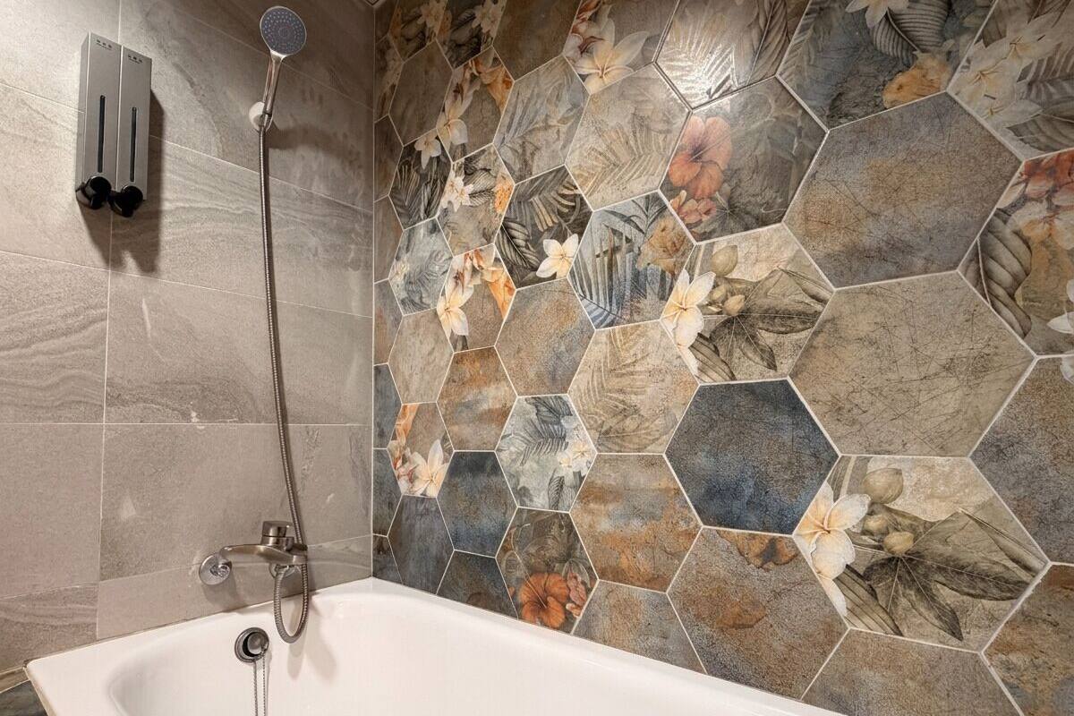 A bathroom with a white bathtub, a shower with a handheld showerhead, and a wall with hexagonal tiles featuring floral patterns.