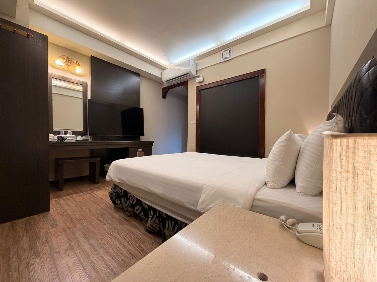 A hotel room with a bed, bedside table, desk, chair, and a large mirror.