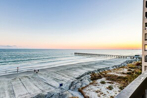 A beach with a pier extending into the ocean, rocky terrain, and a building on the right.