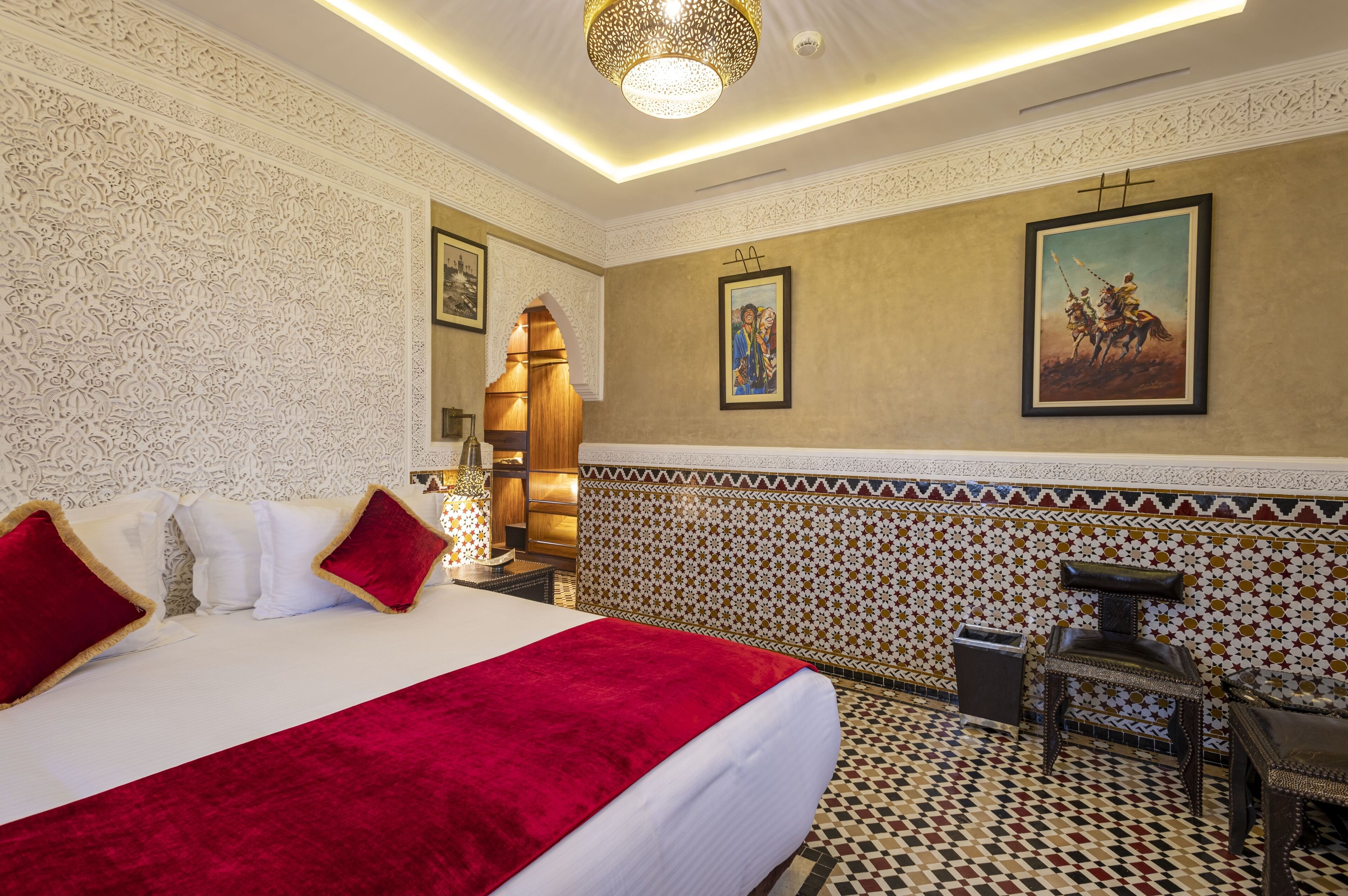 A hotel room with a large bed, a nightstand, a chair, and a wall with intricate patterns and artwork.