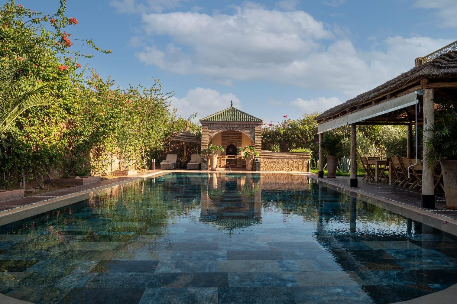 A swimming pool with a covered seating area and a gazebo in the background.