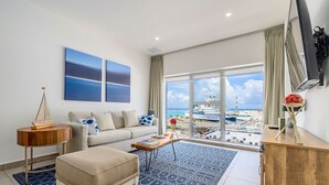 Un salon moderne avec une grande fenêtre, un canapé, une table basse et une vue sur un navire de croisière.