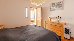 A bedroom with a bed, a wooden dresser, a wall-mounted air conditioner, and a window with a view of a balcony.