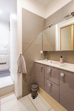 A modern bathroom with a white sink, beige tiles, and a mirror above the vanity. - LE JFK, a contemporary twist on the old (Dijon)