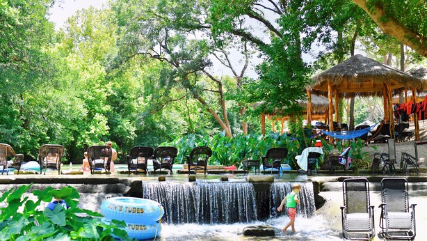 A water feature with chairs and a thatched-roof structure in a lush, green setting. - 19 Son's Rio Cibolo - Birdhouse Cabin (Marion)