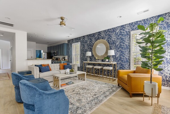A modern living room with a sofa, coffee table, and chairs, a dining area with a table and chairs, and a kitchen in the background.