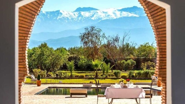 A dining area with a table set for two, overlooking a pool and a mountainous landscape. - Domaine Marrakech Hacienda a great place to party (Marrakech)