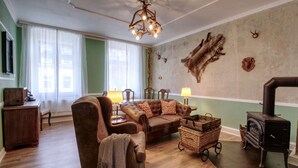 A cozy living room with a fireplace, a plush armchair, a sofa, and a wooden cabinet. - Vacation apartment Herrenzimmer with fireplace and terrace (Annaberg-Buchholz)
