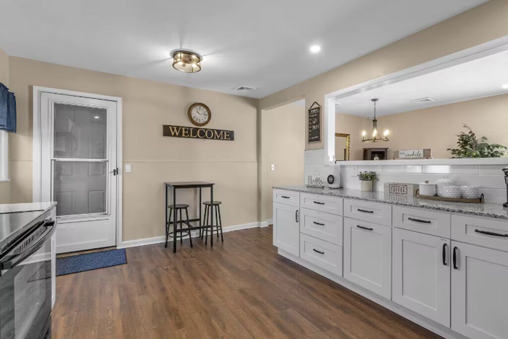 A kitchen with white cabinets, a wooden floor, a welcome sign, and a clock on the wall.