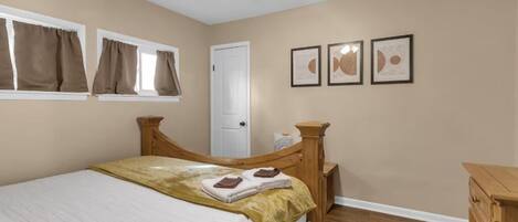 A bedroom with a bed, a wooden headboard, a ceiling fan, a window with curtains, and a door.