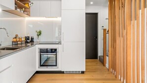 Une cuisine moderne avec des meubles blancs, un four encastré et une cloison en bois.
