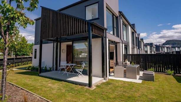 Une maison moderne à deux étages, dotée d’un patio, de grandes fenêtres et offrant une vue sur le paysage environnant.