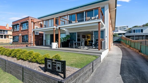 A modern building with a flat roof, large windows, and a covered outdoor seating area.