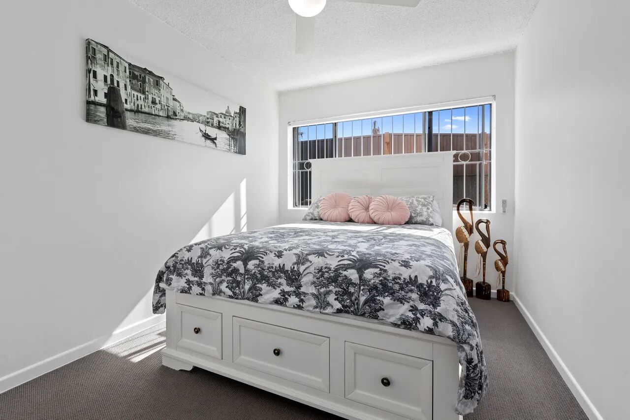 A bedroom with a bed, a window with bars, a painting on the wall, and a staircase leading to another room.