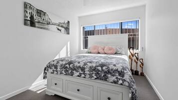A bedroom with a bed, a window with bars, a painting on the wall, and a staircase leading to another room.