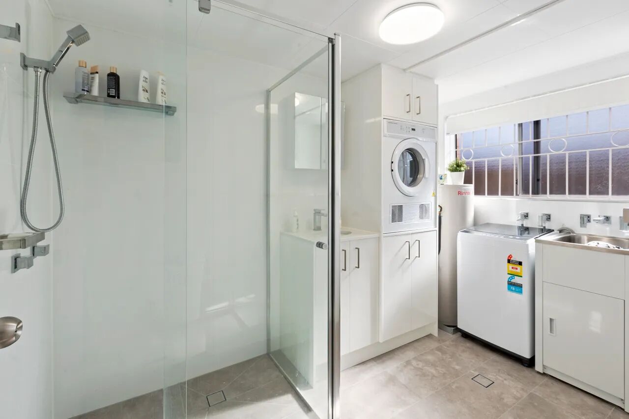 A modern bathroom with a glass shower enclosure, a built-in washing machine, and a sink with a countertop.