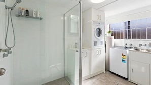 A modern bathroom with a glass shower enclosure, a built-in washing machine, and a sink with a countertop.