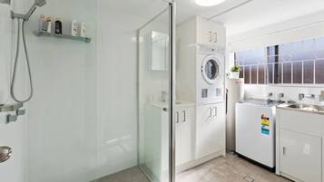 A modern bathroom with a glass shower enclosure, a built-in washing machine, and a sink with a countertop.