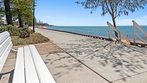 A paved walkway with a bench, trees, and a view of the sea.