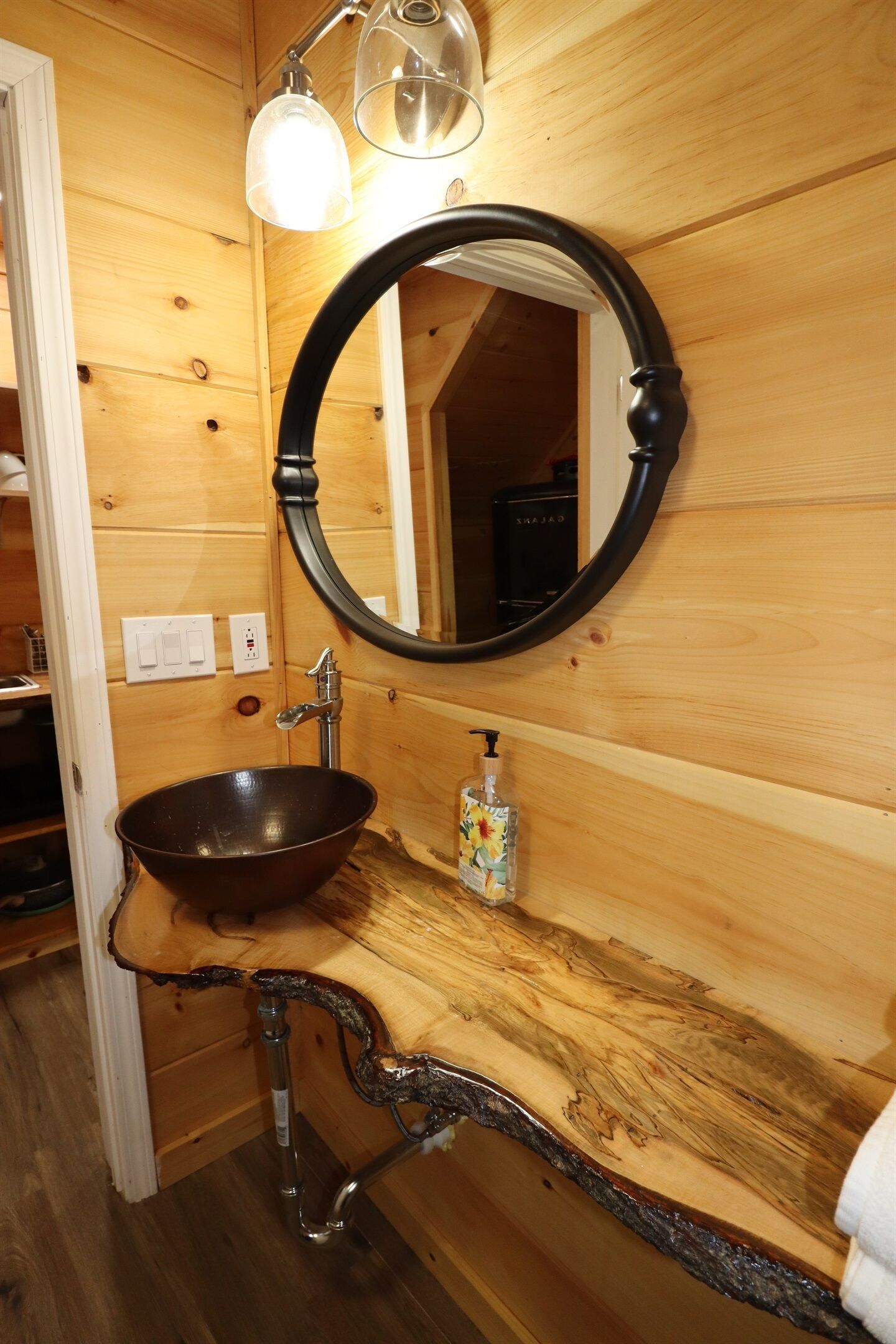 A wooden bathroom with a round mirror, a wooden sink, and a light fixture above the mirror.