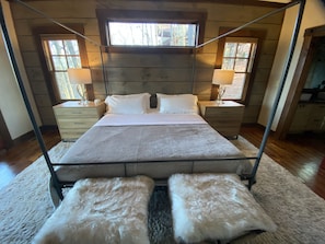 A bedroom with a four-poster bed, wooden headboard, two bedside tables with lamps, and a large window.