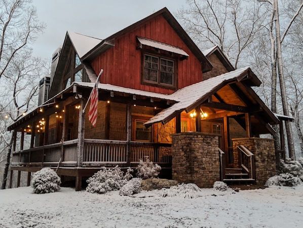 A rustic cabin with a stone foundation, wooden exterior, and a porch with string lights.