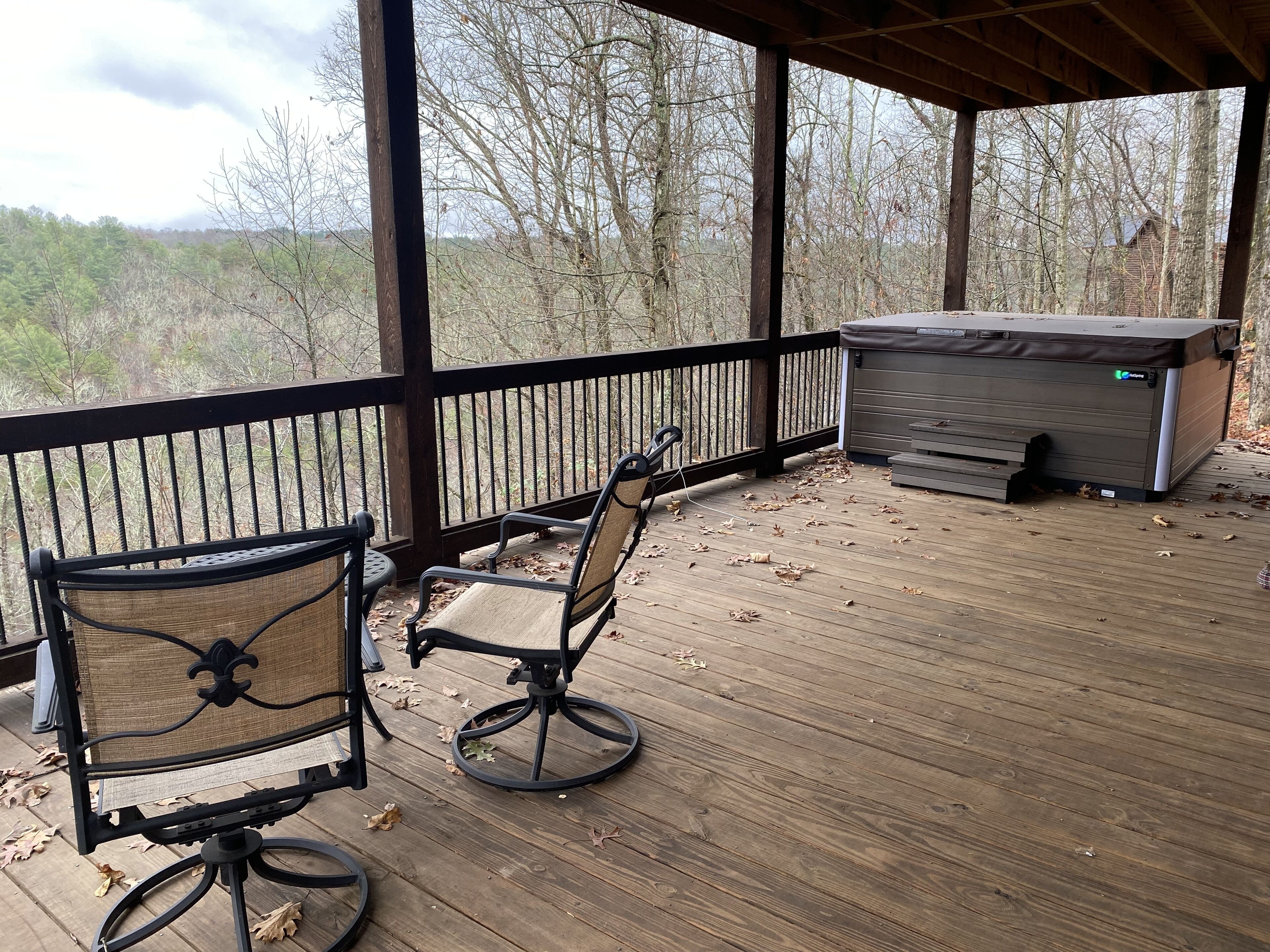 Une terrasse couverte avec deux fauteuils en osier et un jacuzzi.