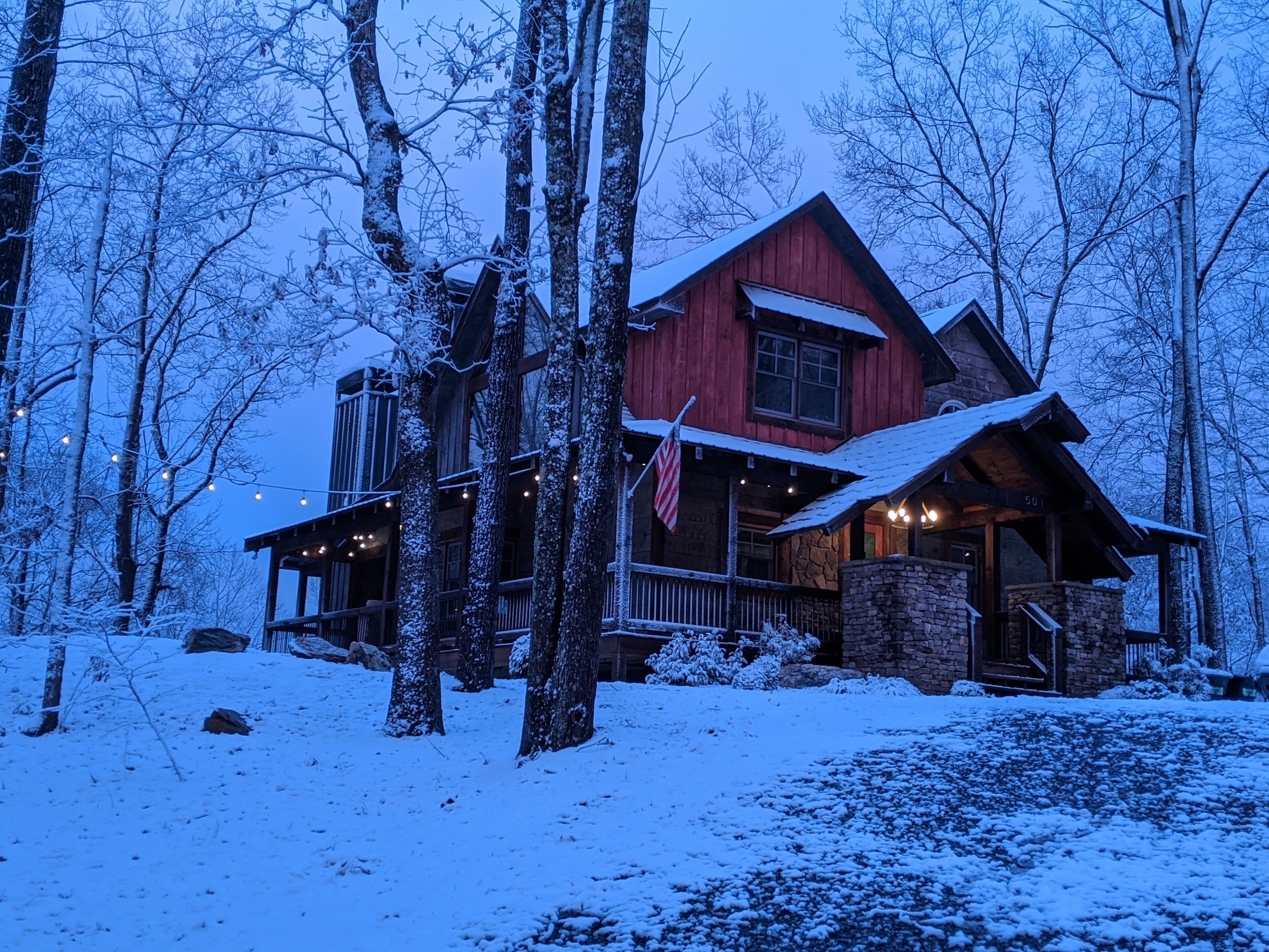 A rustic cabin with a stone foundation, wooden exterior, and a porch with string lights.