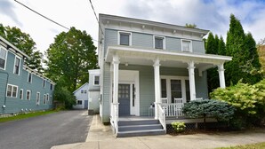 A two-story house with a front porch, a driveway, and a small front yard with a tree.