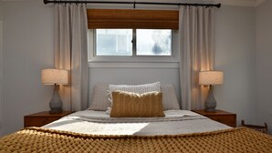 A bedroom with a bed, two bedside lamps, a window with curtains, and a view of the outside.