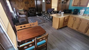 Une pièce confortable, aménagée dans le style d’un chalet, avec une table à manger en bois, un canapé et un coin cuisine doté de meubles et d’un plan de travail en bois.