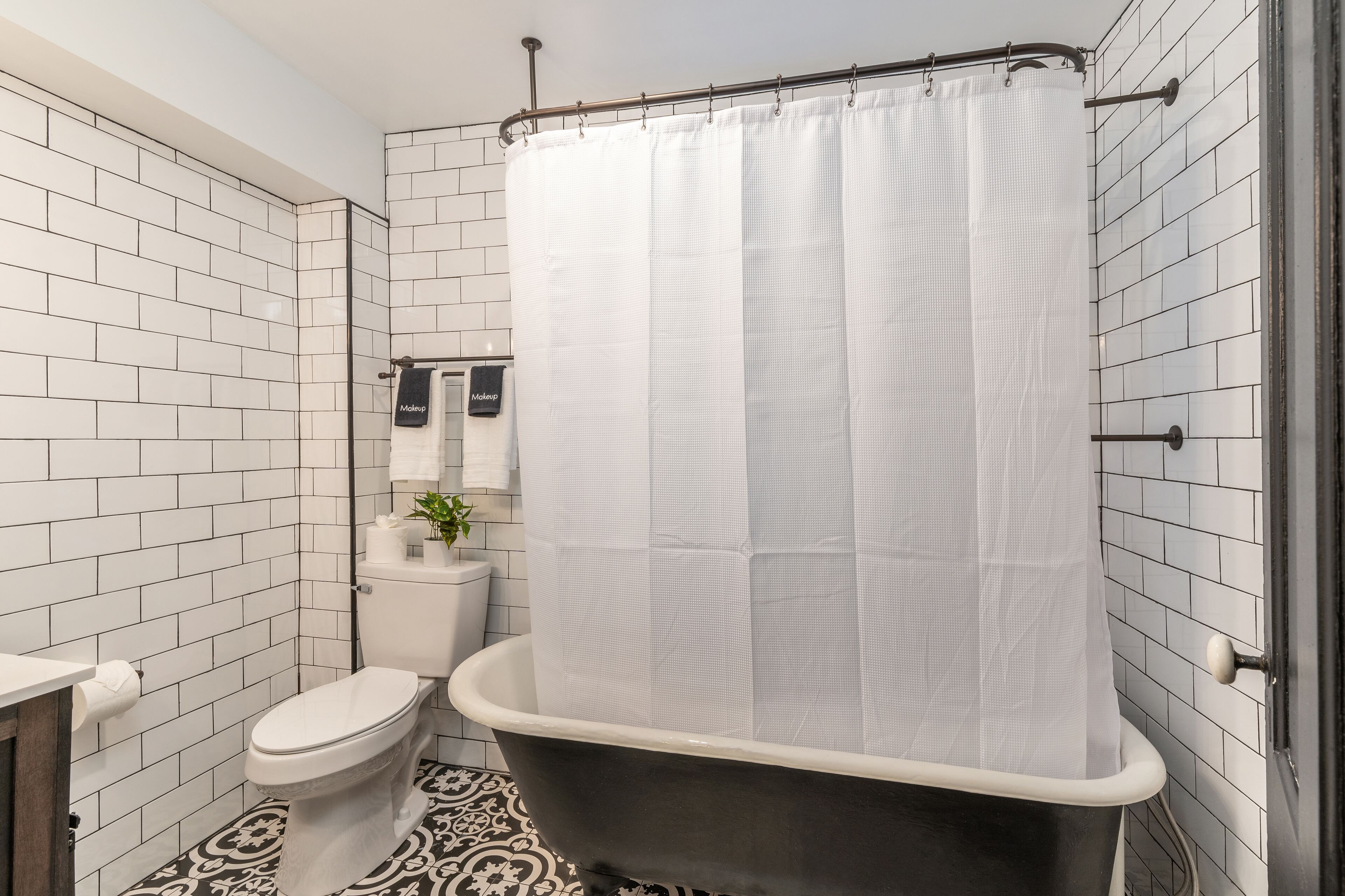 A bathroom with white tiled walls, a black bathtub, a toilet, and a shower curtain.