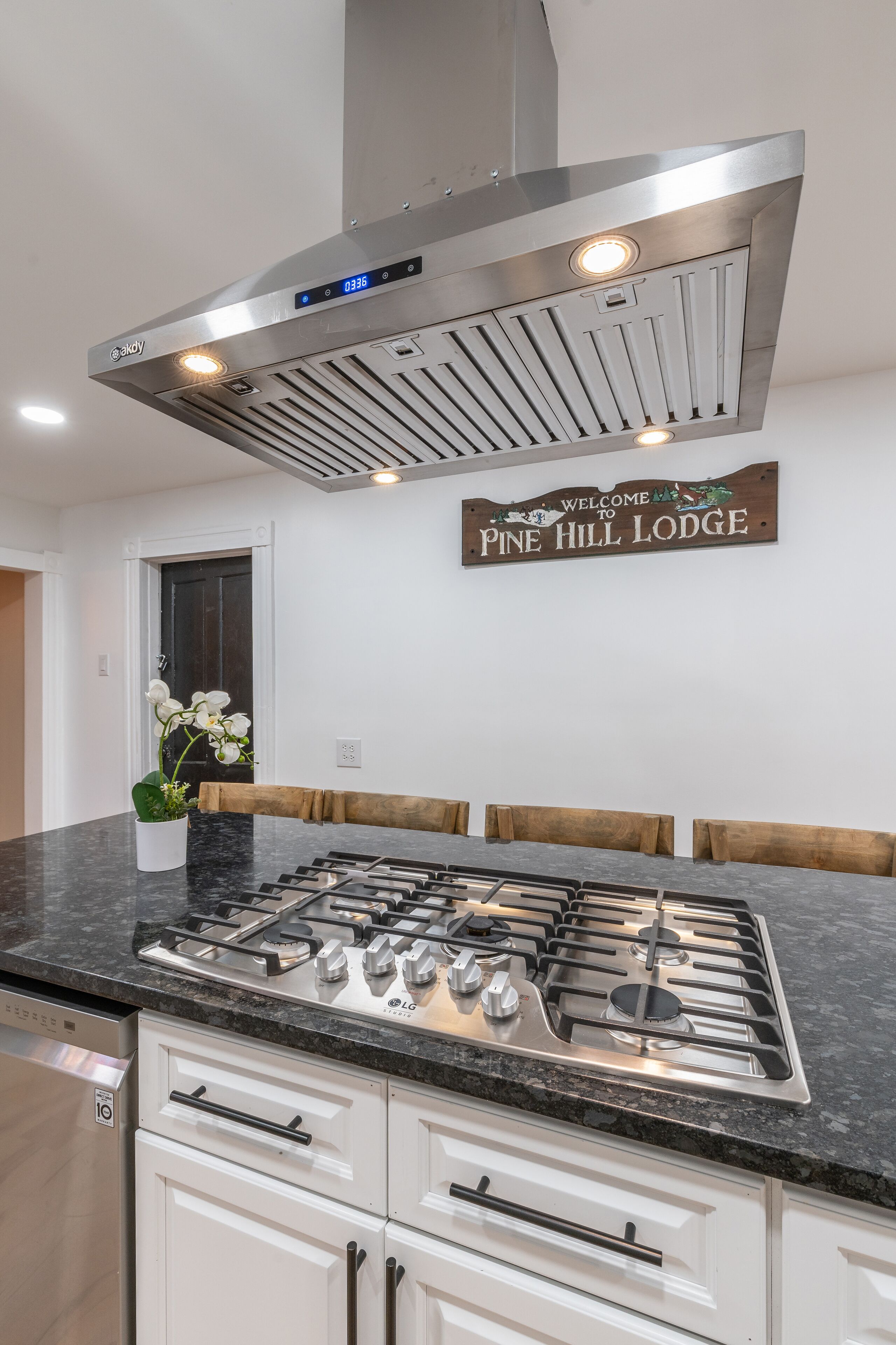 A kitchen with a stainless steel range hood, a digital clock, and a welcome sign for Pine Hill Lodge.
