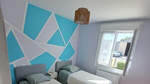 Un dormitorio con dos camas, un diseño geométrico en la pared, una lámpara colgante y una ventana con vistas al exterior.