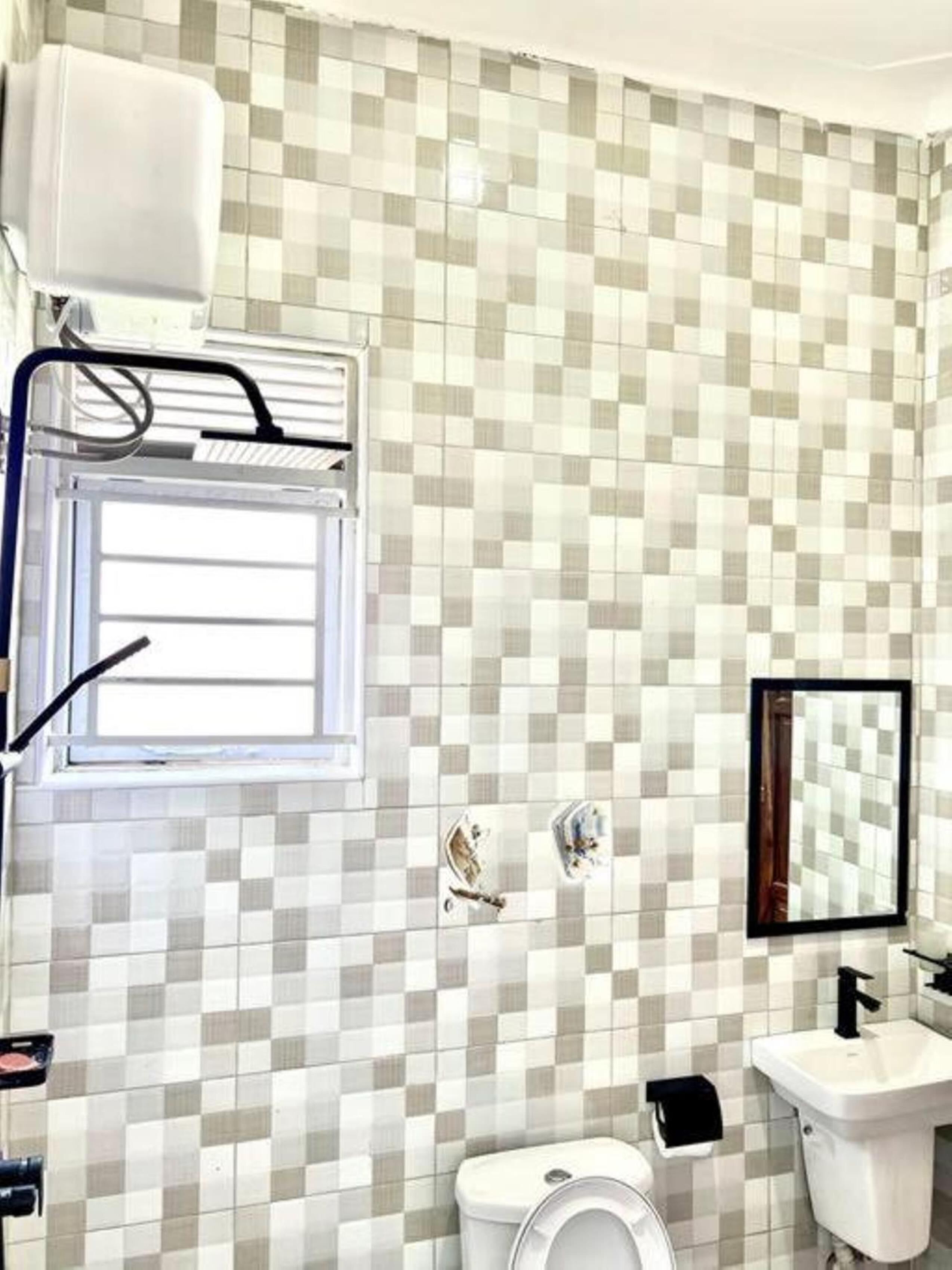 A bathroom with a checkered tile backsplash, a window, a sink, and a toilet.