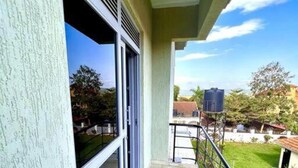 A balcony with a view of a grassy area and a water tank in the background. - C&A Orchid Apartments (Kampala)