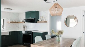 Una cocina moderna con armarios verde oscuro, una mesa de comedor de madera y una lámpara colgante.