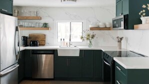 Una cocina moderna con gabinetes verde oscuro, lavavajillas de acero inoxidable y salpicadero de mármol blanco.