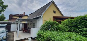 A residential house with a covered patio, a car parked in front, and lush greenery around. - Holiday home in popular holiday area with terrace (Siófok)